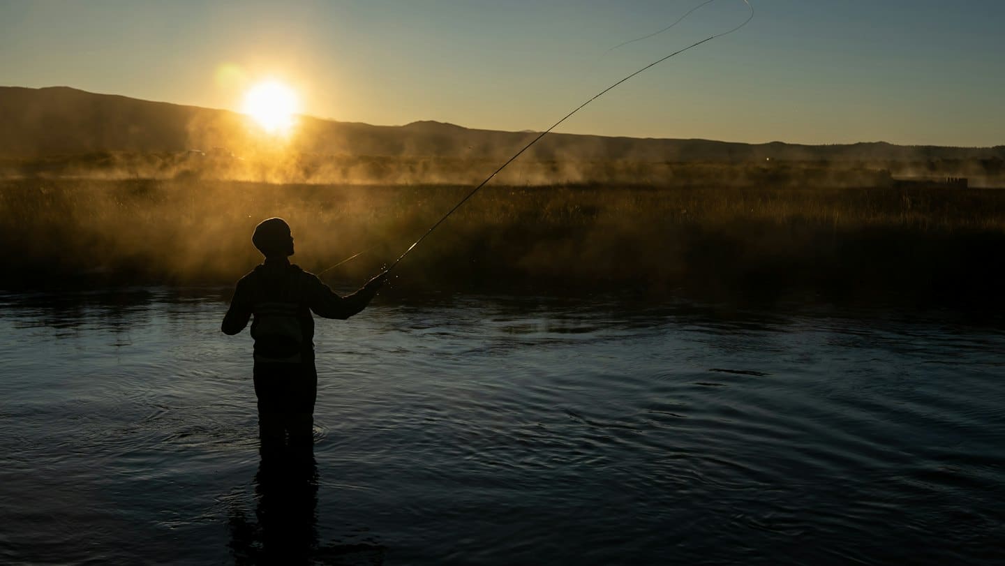 A person fly fishing in a river at sunrise.