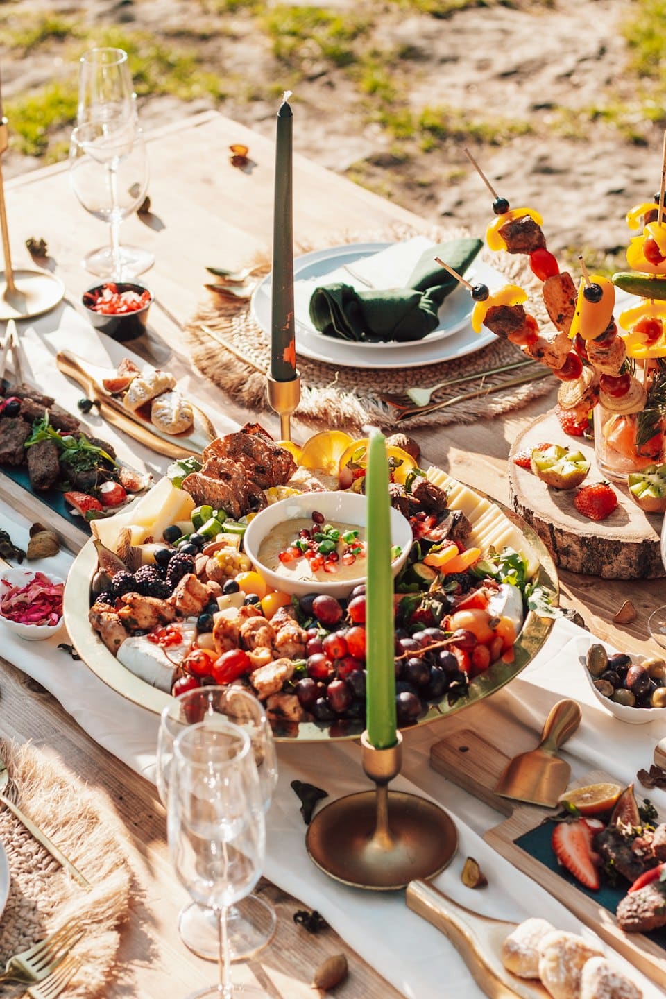 Outdoor picnic spread with charcuterie, fruit, and wine.