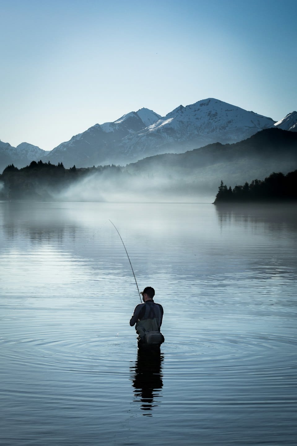 Man fly-fishing in a lake with mountains behind.