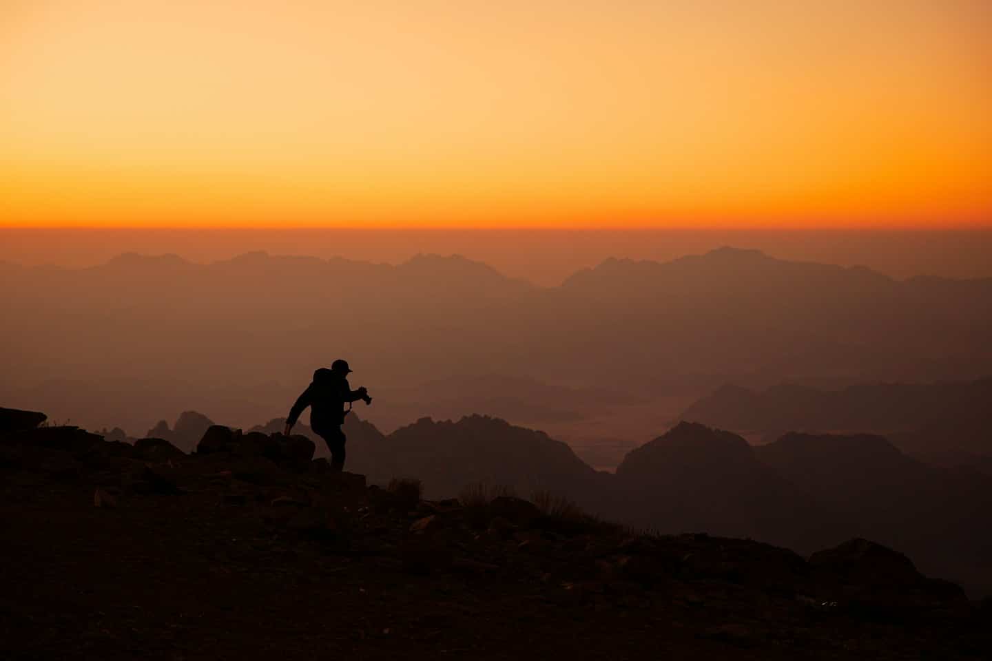 Hiker silhouetted against a vibrant sunrise on a rocky mountain path.